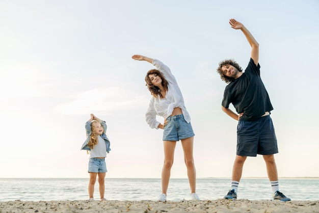 Retrato de corpo inteiro de família feliz fazendo exercícios matinais na praia