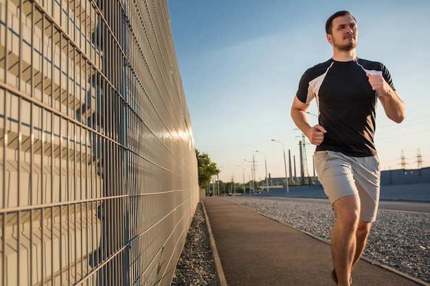 Retrato de corpo inteiro de homem atlético correndo ao ar livre bela parede cinza, construção muscular jovem corredor malhando enquanto corre no parque. Pôr do sol