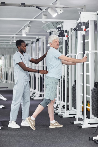 Retrato de corpo inteiro de homem sênior fazendo exercícios de fisioterapia no ginásio na clínica de reabilitação com