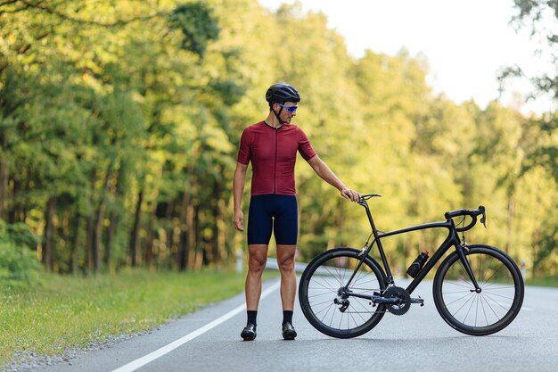 Retrato de corpo inteiro de jovem com pernas fortes, posando com sua bicicleta preta