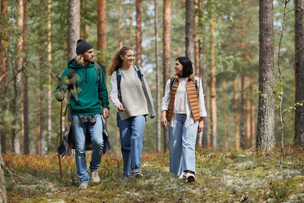 Retrato de corpo inteiro de jovens caminhando na floresta com mochilas enquanto desfrutam de trilhas para caminhadas c ...