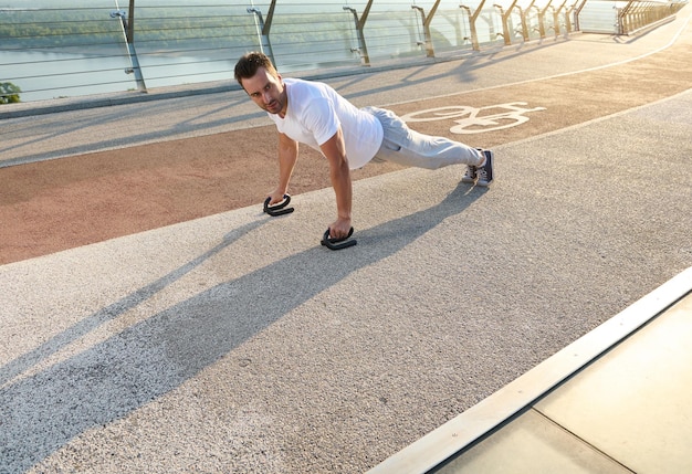 Retrato de corpo inteiro de um belo homem europeu de meia idade, atleta de construção muscular fazendo flexões durante um treino ao ar livre na ponte da cidade no início da manhã