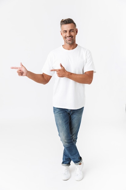 Retrato de corpo inteiro de um homem bonito e casual isolado no branco, apresentando o espaço da cópia, apontando