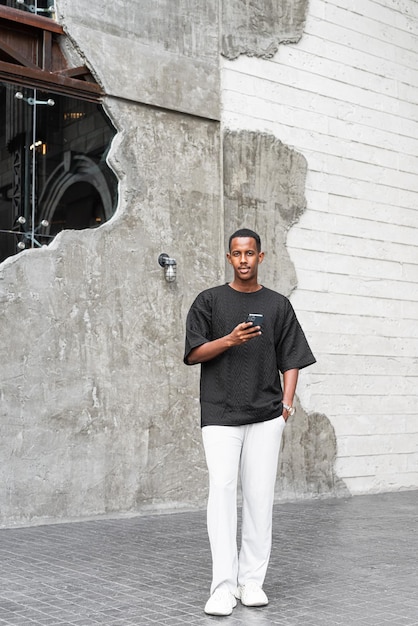 Retrato de corpo inteiro de um jovem africano bonito usando telefone ao ar livre