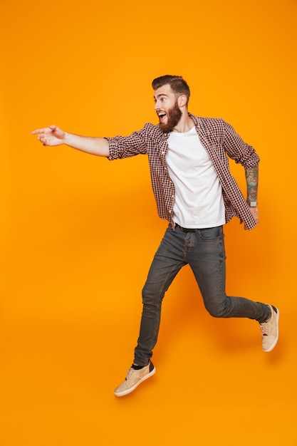 Retrato de corpo inteiro de um jovem alegre, vestindo roupas casuais, fugindo