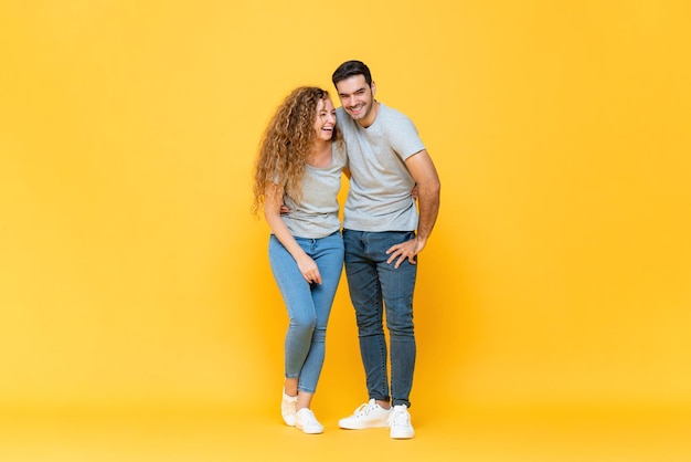 Retrato de corpo inteiro de um jovem casal milenar inter-racial feliz, abraçando-se e rindo em fundo de estúdio amarelo isolado