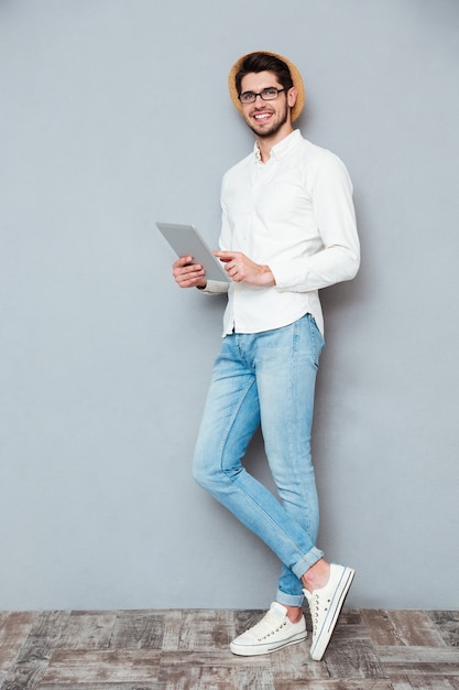 Retrato de corpo inteiro de um jovem feliz usando um computador tablet isolado