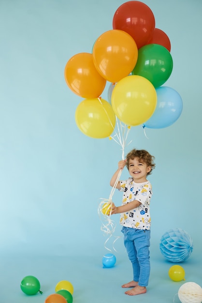 Retrato de corpo inteiro de um menino alegre segurando balons posando contra um fundo azul, conceito de festa de aniversário