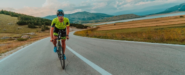 Retrato de corpo inteiro de um triatleta ativo em roupas esportivas e com um capacete protetor andando de bicicleta. Foco seletivo.