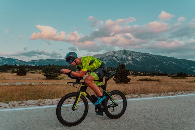 Retrato de corpo inteiro de um triatleta ativo em roupas esportivas e com um capacete protetor andando de bicicleta. Foco seletivo.