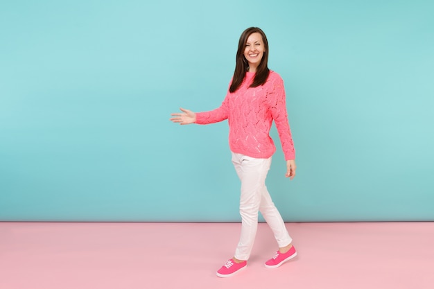 Retrato de corpo inteiro de uma jovem sorridente em um suéter de malha rosa, calças brancas posando