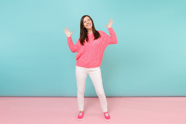 Retrato de corpo inteiro de uma jovem sorridente em um suéter de malha rosa, calças brancas posando