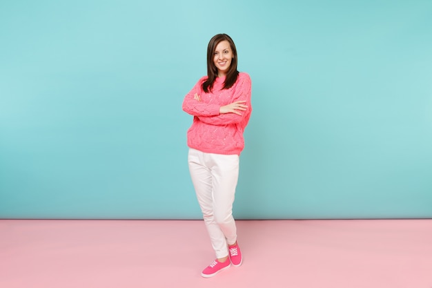 Retrato de corpo inteiro de uma jovem sorridente em um suéter de malha rosa, calças brancas posando