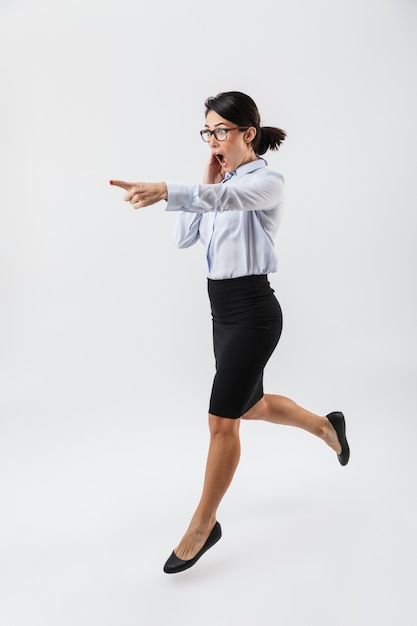 Retrato de corpo inteiro de uma linda mulher de negócios pulando isolada na parede branca, comemorando o sucesso, apontando para longe