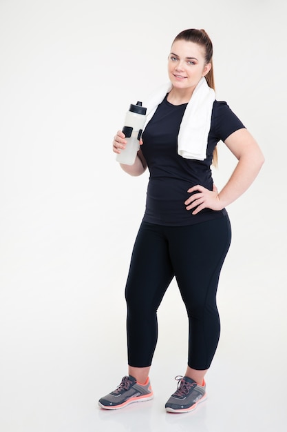 Retrato de corpo inteiro de uma mulher gorda em roupas esportivas segurando um shaker isolado em uma parede branca