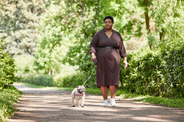 Retrato de corpo inteiro de uma mulher madura elegante usando vestido enquanto caminhava com o cachorrinho no spa de cópia do parque