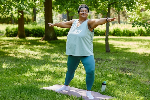 Retrato de corpo inteiro de uma mulher negra com excesso de peso malhando ao ar livre no parque e sorrindo espaço de cópia