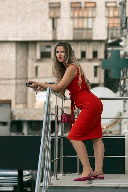 Retrato de corpo inteiro de uma mulher sexy loira atraente de vestido vermelho na paisagem urbana Mulher de negócios Quadro vertical