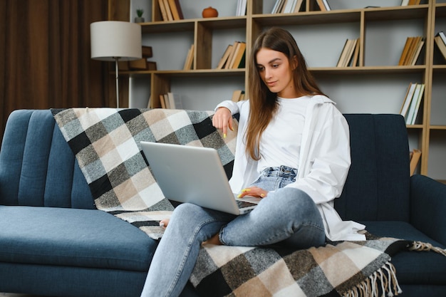 Retrato de corpo inteiro de uma pessoa alegre e encantadora sentada segurando netbook navegando tem bom humor trabalhando em casa dentro de casa