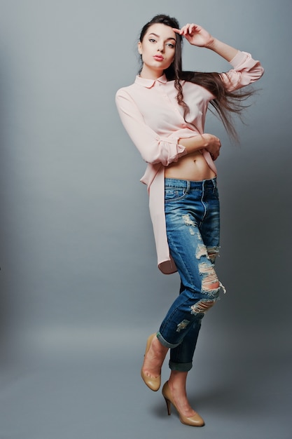 Retrato de corpo inteiro jovem menina morena sexy mostrando seu umbigo, vestindo blusa rosa, jeans rasgados e sapatos creme