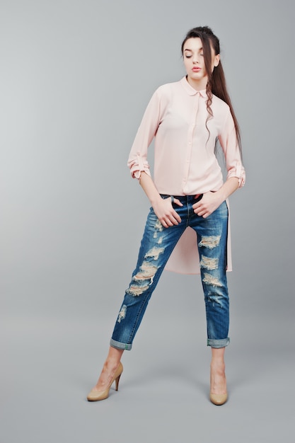 Retrato de corpo inteiro jovem menina morena vestindo blusa rosa, jeans rasgados e sapatos creme