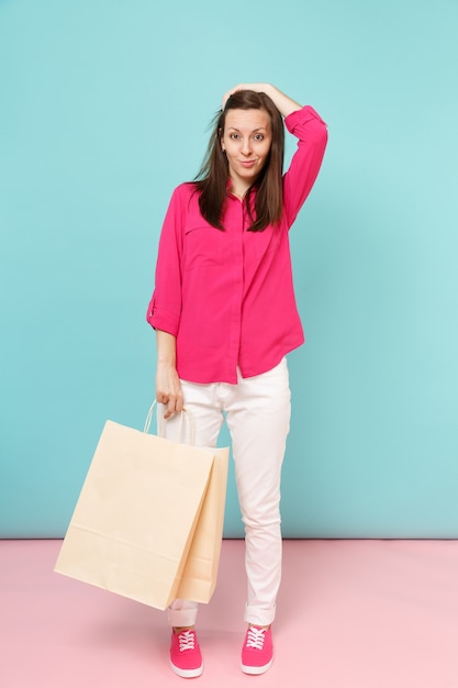 Retrato de corpo inteiro sorridente jovem de blusa de camisa rosa, calça branca segurar sacolas de compras isoladas na parede pastel azul rosa brilhante.