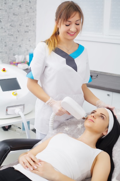 Retrato de cosmetologista feminina com cliente jovem em roupão sentado no escritório cosmetologista