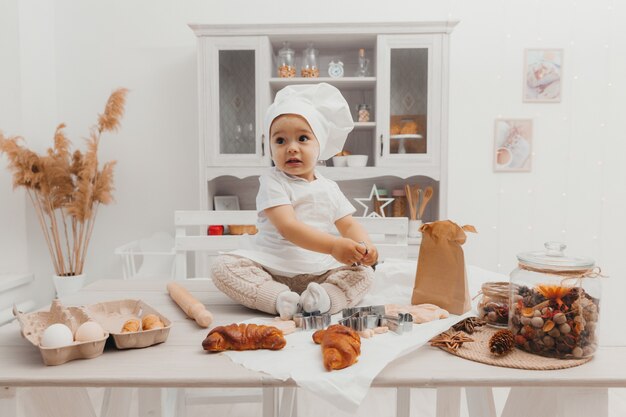 Retrato de criança adorável caucasiano com um chapéu de chef. Bebê fofo está sentado na cozinha em casa.