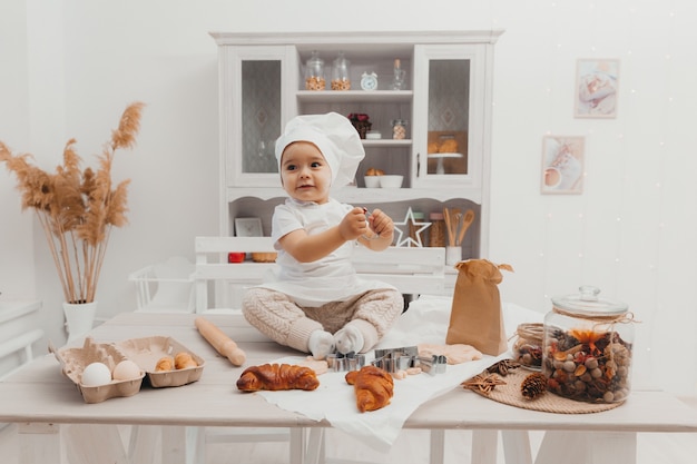 Retrato de criança adorável caucasiano com um chapéu de chef. bebê fofo está sentado na cozinha em casa.