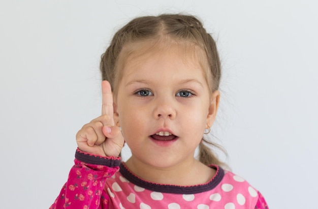 Foto retrato de criança caucasiana de três anos segurando o dedo para mostrar o número um ou contar a importância olhando para a câmera no fundo branco
