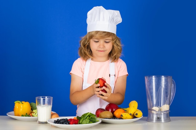 Retrato de criança chef com chapéu de cozinheiro cozinhando em casa garoto preparando comida de vegetais e frutas