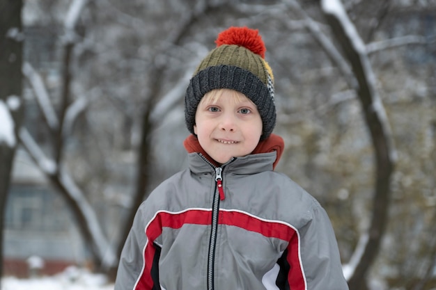 Retrato de criança com chapéu de inverno contra o fundo do quintal de neve.