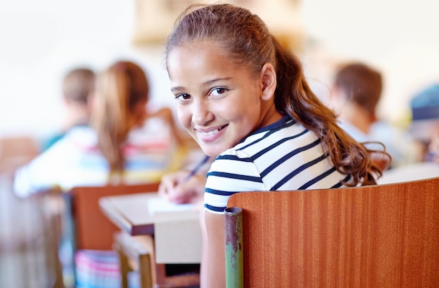 Retrato de criança e mesa de escola na sala de aula com caderno ou lição estudando em academia ou educação aprender ou conhecimento Aluno de pessoa feminina e lápis com sorriso para escrever exame de teste ou escrever
