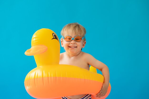 Retrato de criança feliz com pato de borracha amarelo contra parede azul.