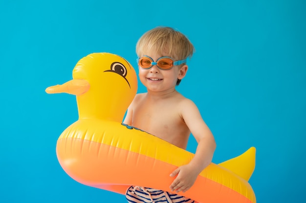 Retrato de criança feliz com pato de borracha amarelo contra parede azul.