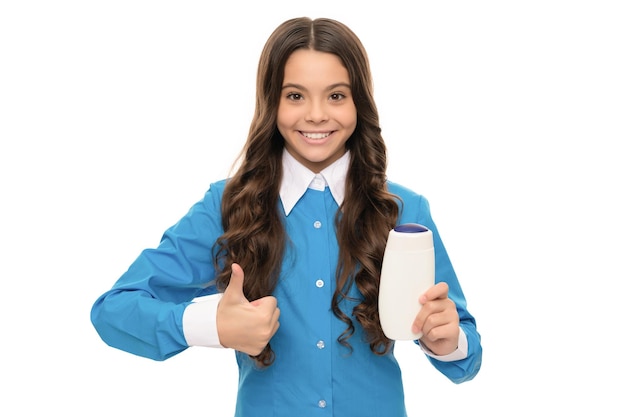 Retrato de criança feliz tem cabelo longo encaracolado segurando garrafa de condicionador de cabelo isolada em branco mostrando o polegar para cima de queratina