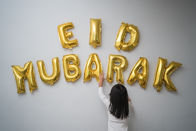 Retrato de criança muçulmana decorando carta de eid mubarak feita de decoração de balão contra a parede em casa