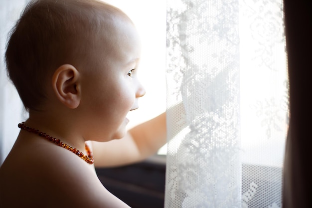 Retrato de criança olhando para a janela pela manhã Um menino usando colar de âmbar conceito de dentição indolor analgésico natural