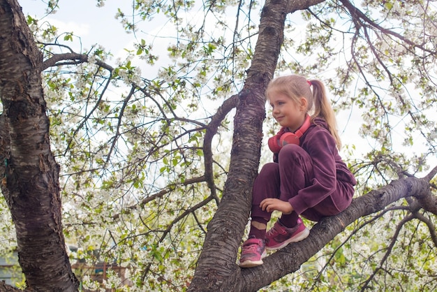 Retrato de criança sentada na grande e velha árvore florescendo no dia da primavera Criança subindo em uma árvore