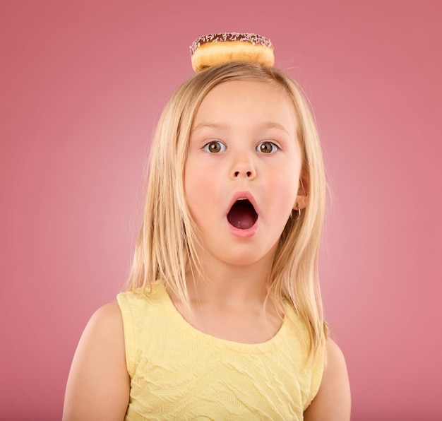 Retrato de criança uau e rosquinha em estúdio com surpresa na cabeça em um fundo rosa Rosto de uma modelo infantil com boca aberta chocada e lanche cômico de chocolate isolado em cor e espaço criativos