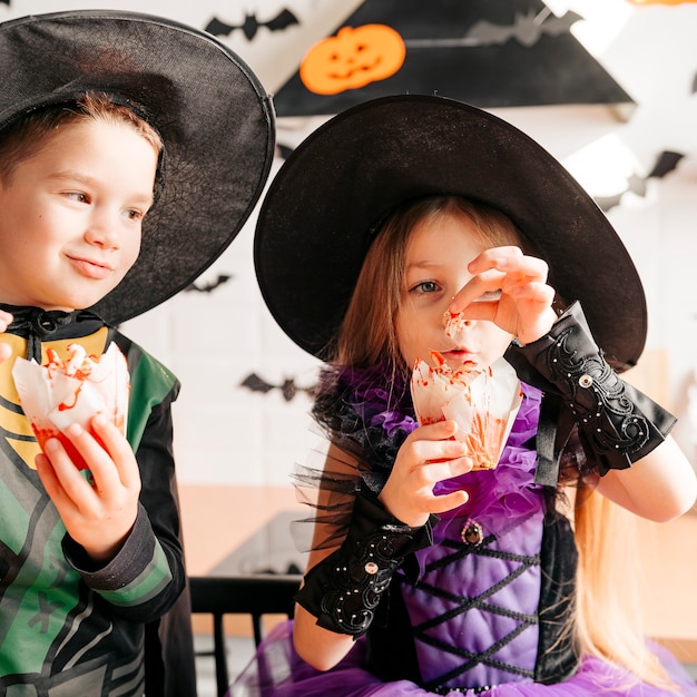 Foto retrato de crianças em fantasias de halloween comendo doces e salgadinhos enquanto festejavam em uma cozinha decorada