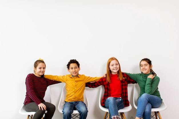 Retrato de crianças fofas em jeans, sentadas em cadeiras contra a parede branca