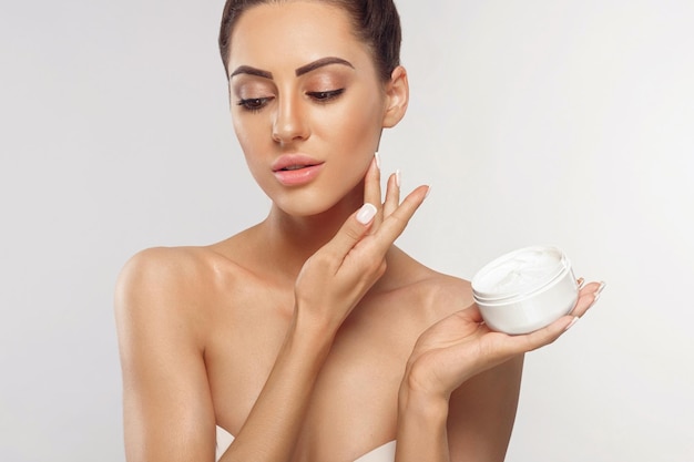 Retrato de cuidados com a pele de modelo feminino segurando e aplicando creme hidratante cosmético