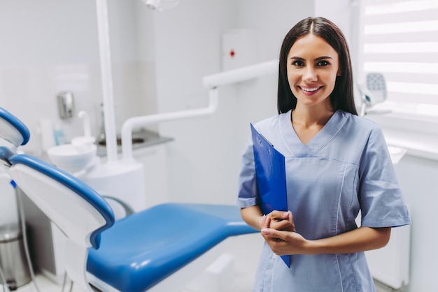 Retrato de dentista feminina sorridente com prancheta no local de trabalho na clínica médica moderna