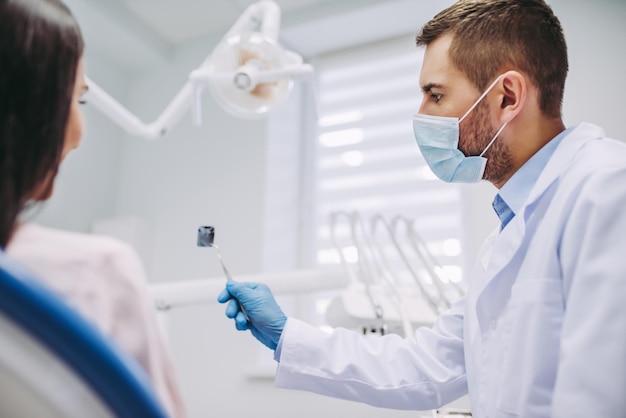 Retrato de dentista mostrando no raio-x para o paciente na clínica moderna