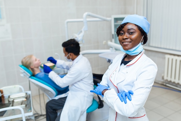 Retrato de dentista negro feminino no consultório odontológico. Ela está em seu escritório e tem um lindo sorriso. Equipamento médico moderno