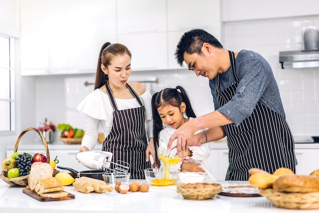 Retrato de desfrutar de amor feliz pai e mãe de família asiática com filha pequena menina asiática se divertindo cozinhando junto com assar biscoitos e ingredientes do bolo na mesa da cozinha
