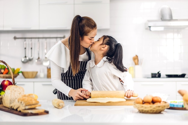 Retrato de desfrutar feliz amor família asiática mãe e filha pequena menina asiática se divertindo cozinhando junto com assar biscoitos e ingredientes do bolo na mesa da cozinha