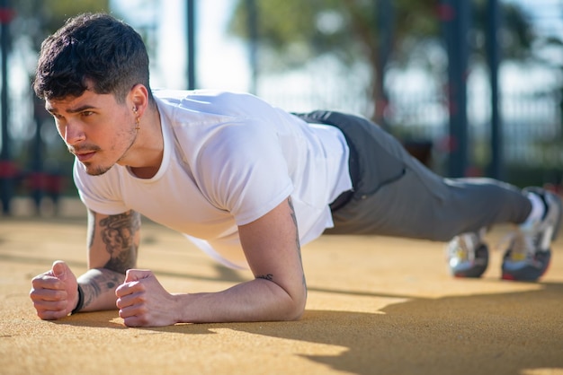 Retrato de desportista bonito em dia de verão. Homem com roupas esportivas fazendo prancha. Esporte, conceito de retrato