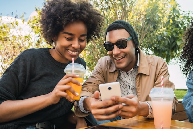 Foto retrato de dois amigos afro usando o celular na cafeteria. conceito de amizade e estilo de vida.